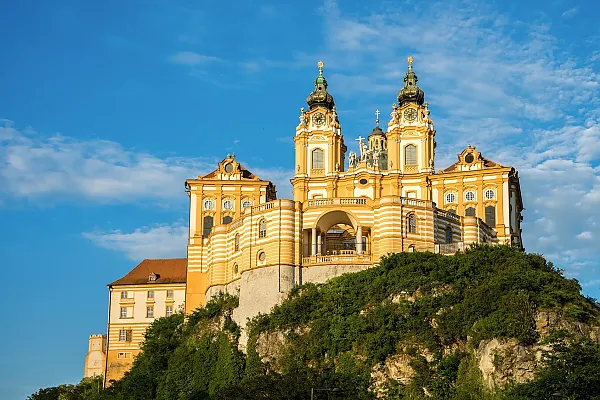 as Bild zeigt das Stift Melk, eine imposante Benediktinerabtei in der österreichischen Stadt Melk. Die Anlage thront auf einem markanten Felsvorsprung mit direktem Blick auf die Donau und die Region Wachau.