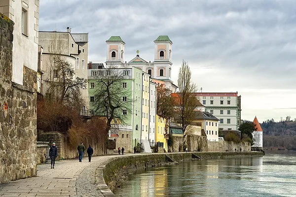 Dieses Bild zeigt die historische Innpromenade in Passau, einer Stadt in Niederbayern, Deutschland.Im Hintergrund ist die markante Kirche St. Michael (auch bekannt als Studienkirche oder Jesuitenkirche) mit ihren zwei Türmen zu sehen.