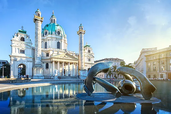 Das Bild zeigt die Wiener Karlskirche am Karlsplatz im 4. Wiener Gemeindebezirk, Wieden. Im Vordergrund, im Wasserbecken des Resselparks, befindet sich die Bronzeskulptur „Hill Arches“ des britischen Bildhauers Henry Moore.