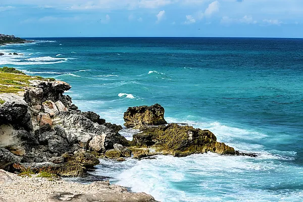 Das Bild zeigt eine felsige Küstenlandschaft mit Klippen und Blick auf das blaue Karibische Meer
